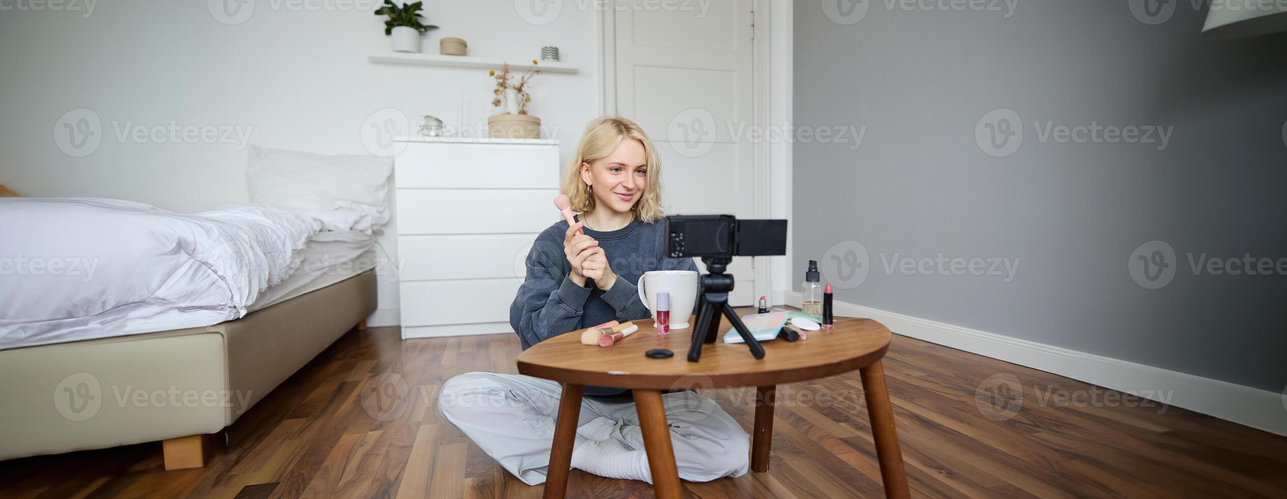 Portrait of beautiful smiling woman, recording in her room, has camera on coffee table, reviewing makeup, doing lifestyle vlog for social media account, records a tutorial photo