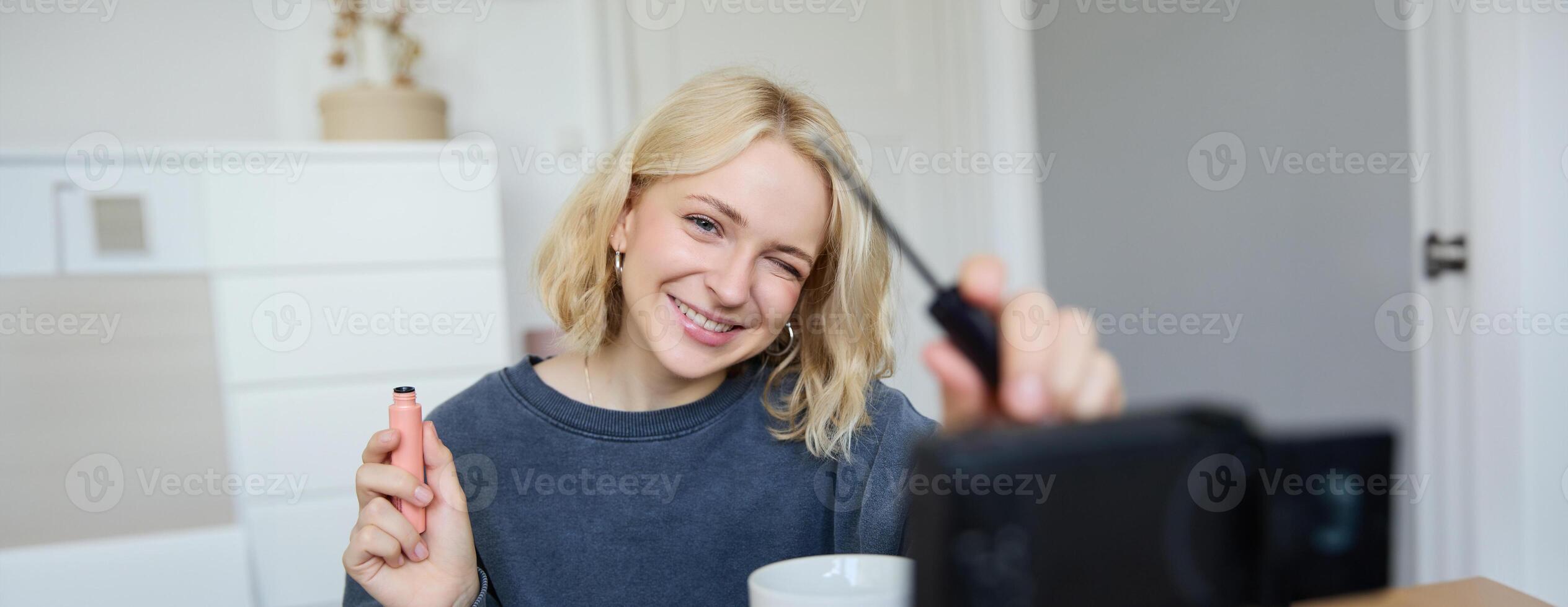 Smiling young beautiful lifestyle blogger, girl records a beauty vlog in her room, using professional camera, showing makeup cosmetics to her followers, creates content for social media photo