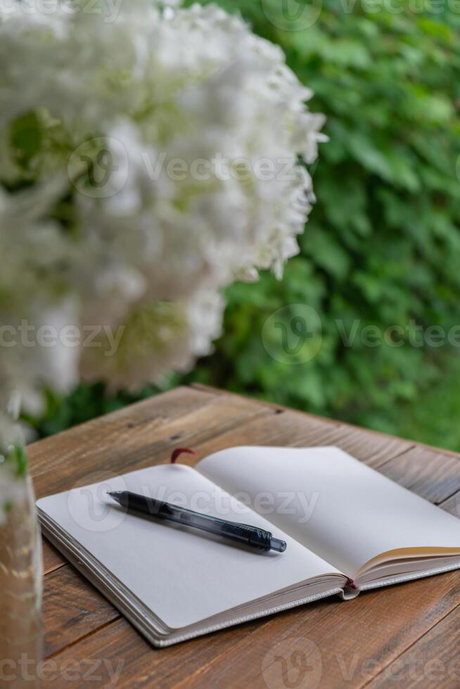 Empty white open paper notebook in wooden table outdoors in garden. Concept of self reflection discovery journal, writing gratitude journal photo