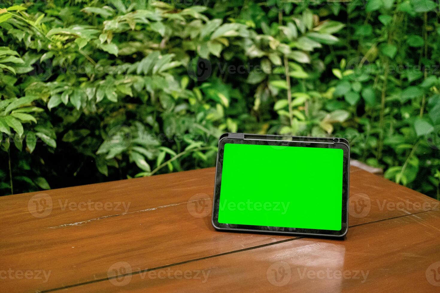Green Screen iPad or Tablet on Wooden Table with Green Plants Background photo
