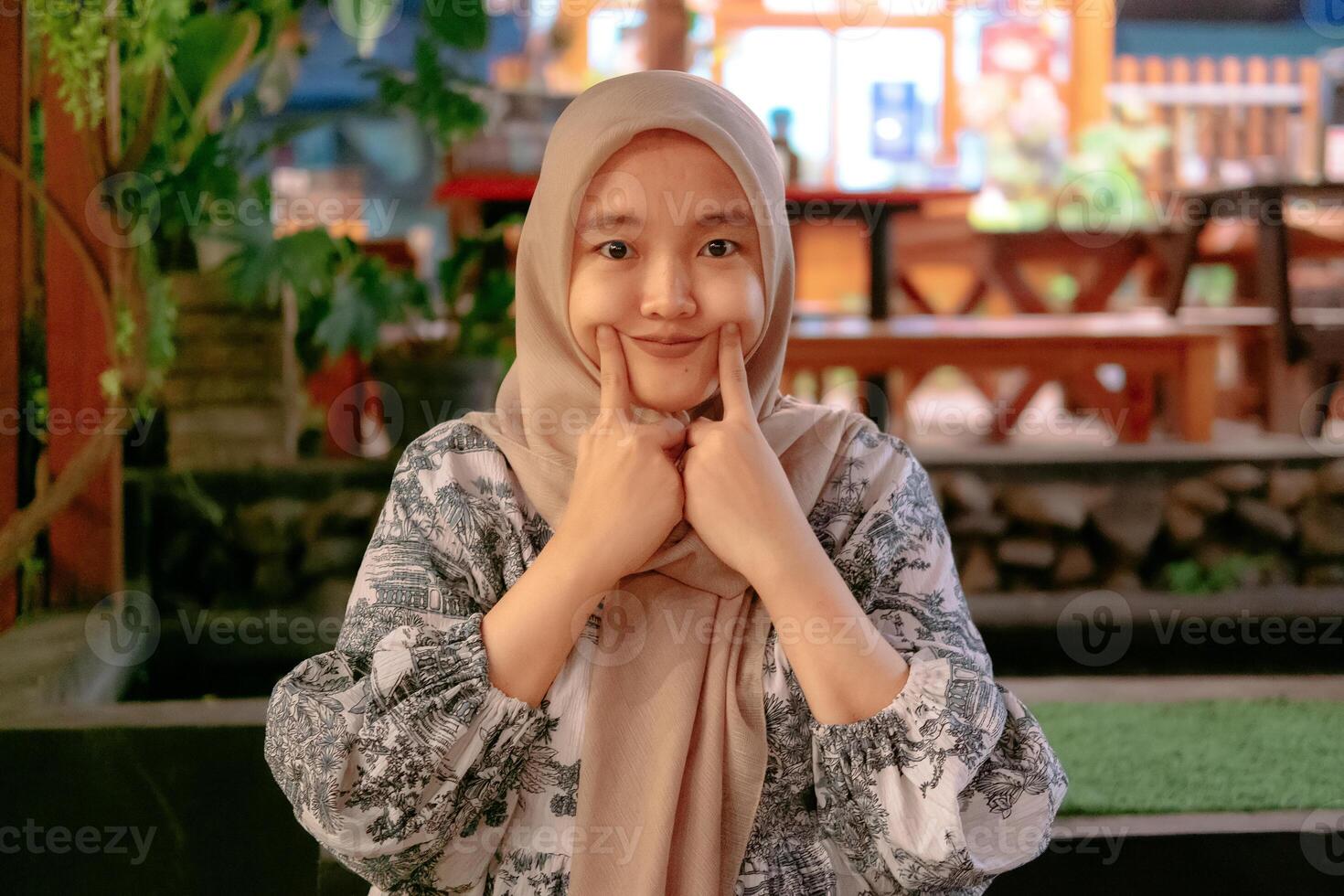 The young Asian woman wearing a hijab with a cute expression against the backdrop of a cafe photo
