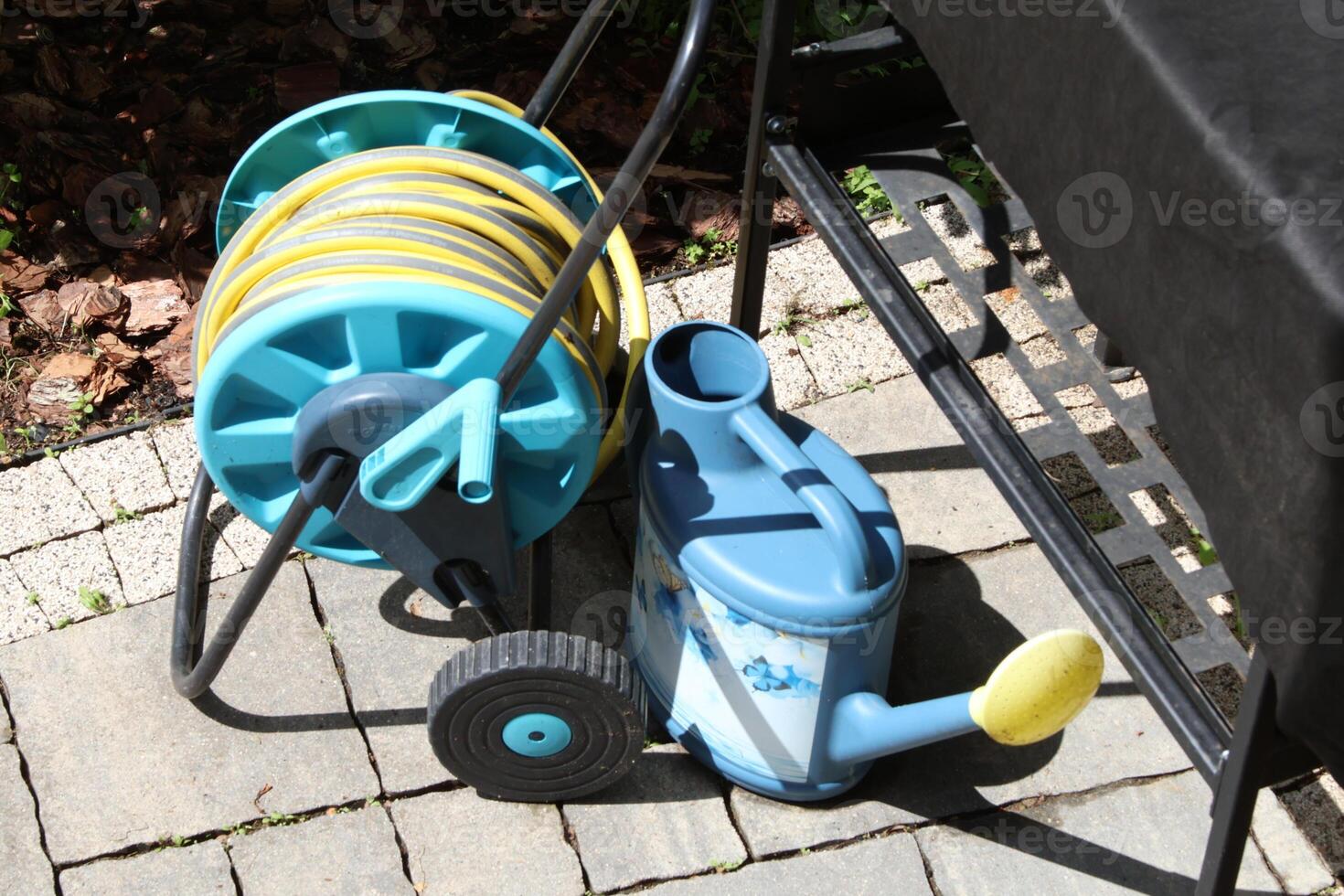 Watering hose on reel, watering can in backyard in spring on stone tile patio. photo