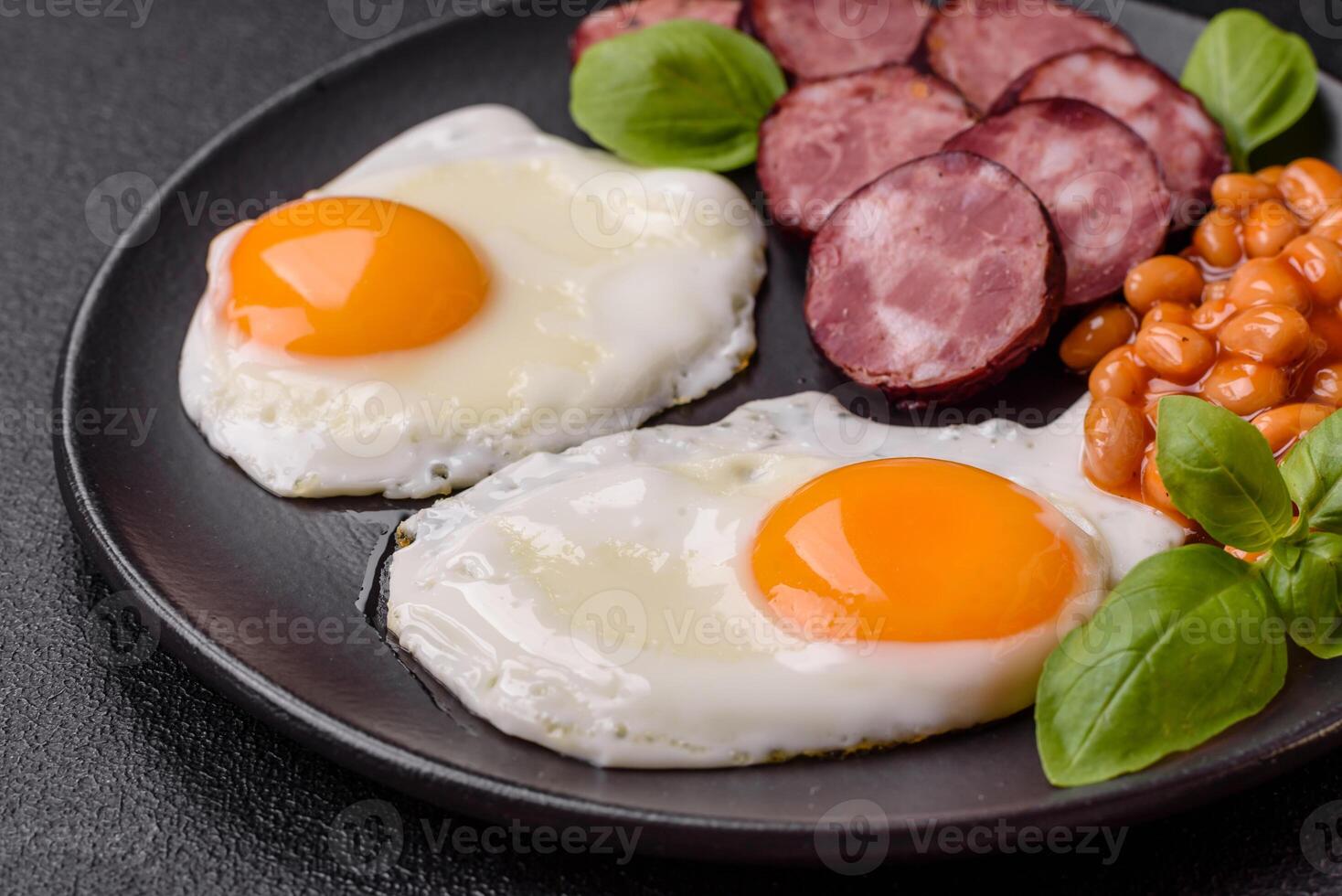 English breakfast with fried eggs, bacon, beans, tomatoes, spices and herbs photo