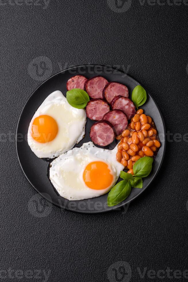 English breakfast with fried eggs, bacon, beans, tomatoes, spices and herbs photo