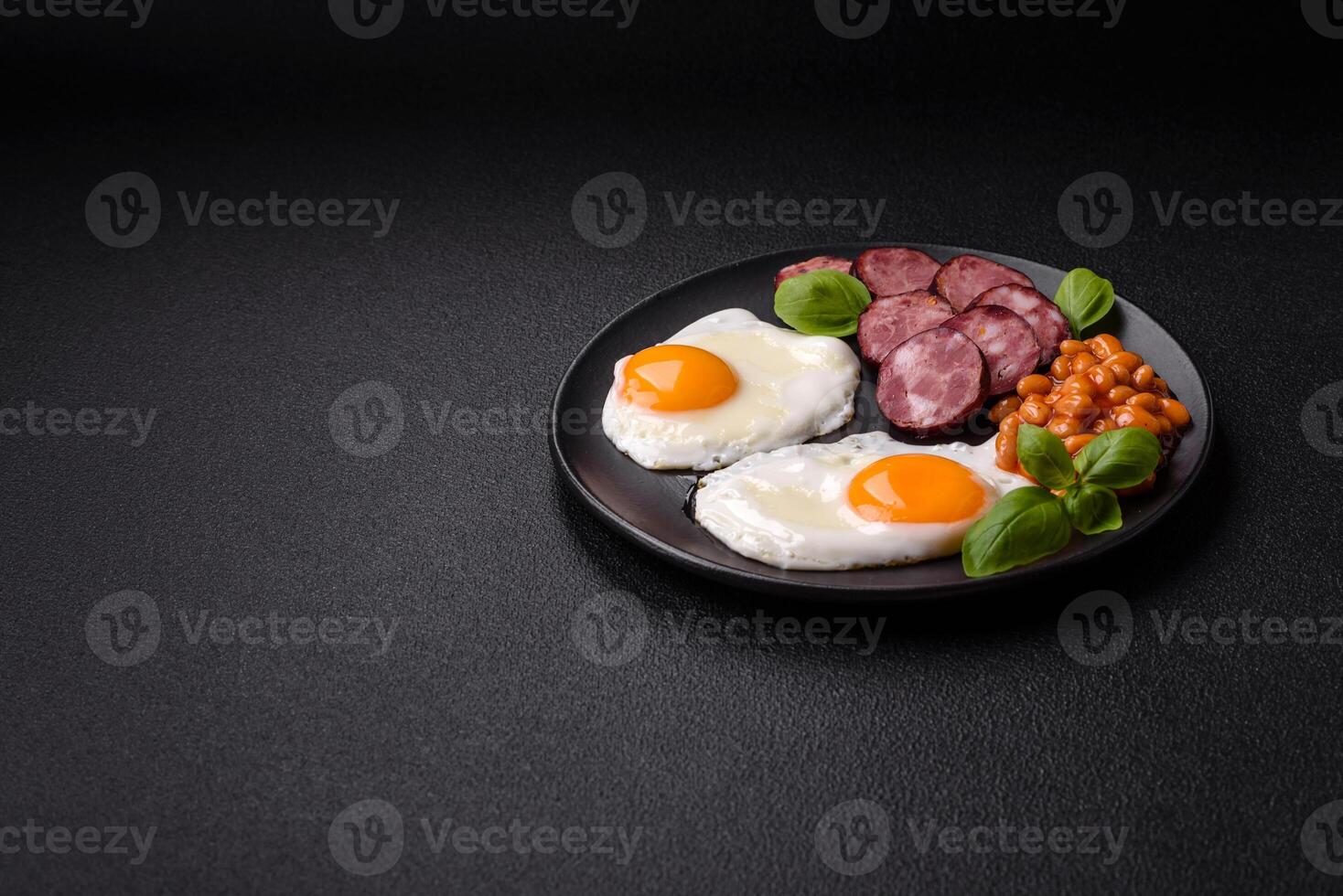 English breakfast with fried eggs, bacon, beans, tomatoes, spices and herbs photo