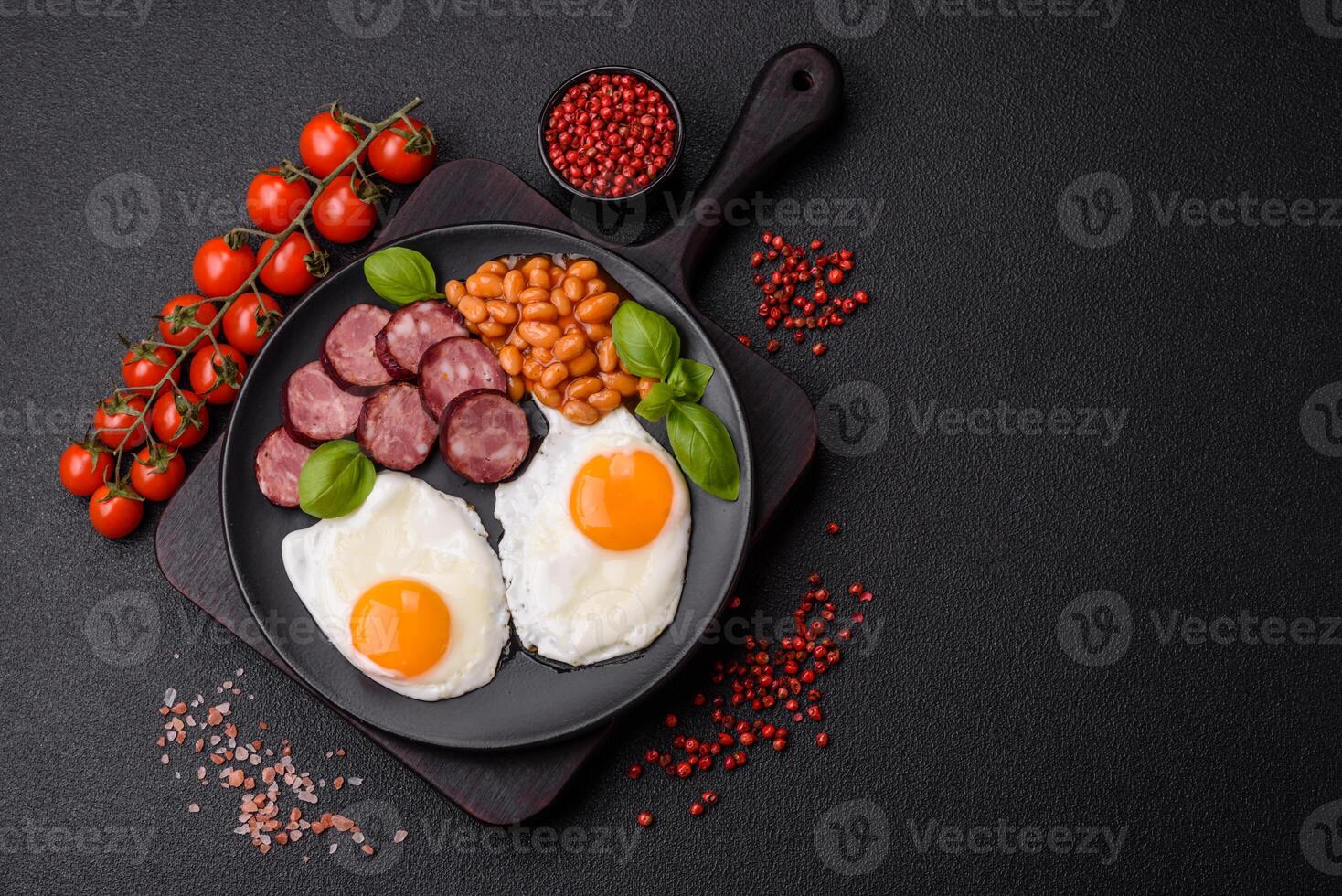 English breakfast with fried eggs, bacon, beans, tomatoes, spices and herbs photo