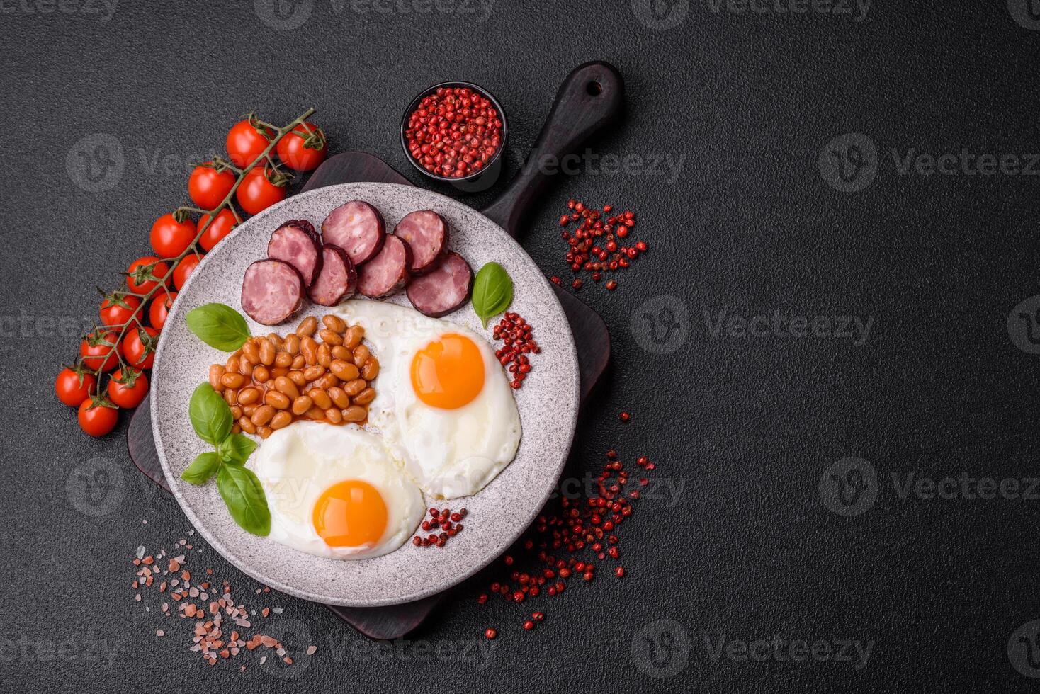 English breakfast with fried eggs, bacon, beans, tomatoes, spices and herbs photo