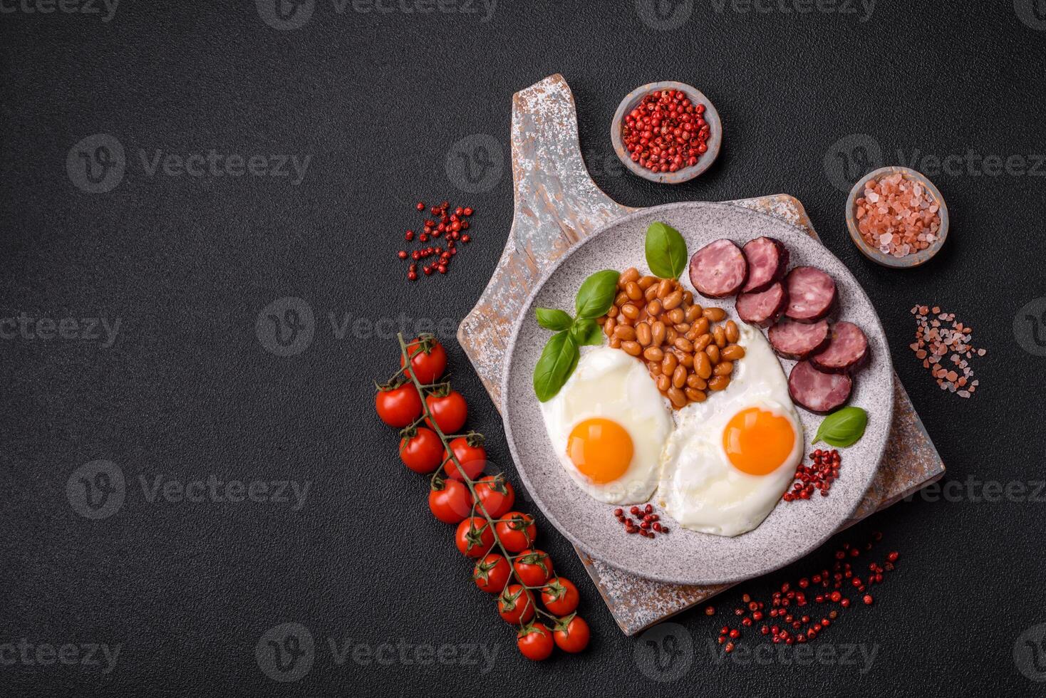 English breakfast with fried eggs, bacon, beans, tomatoes, spices and herbs photo