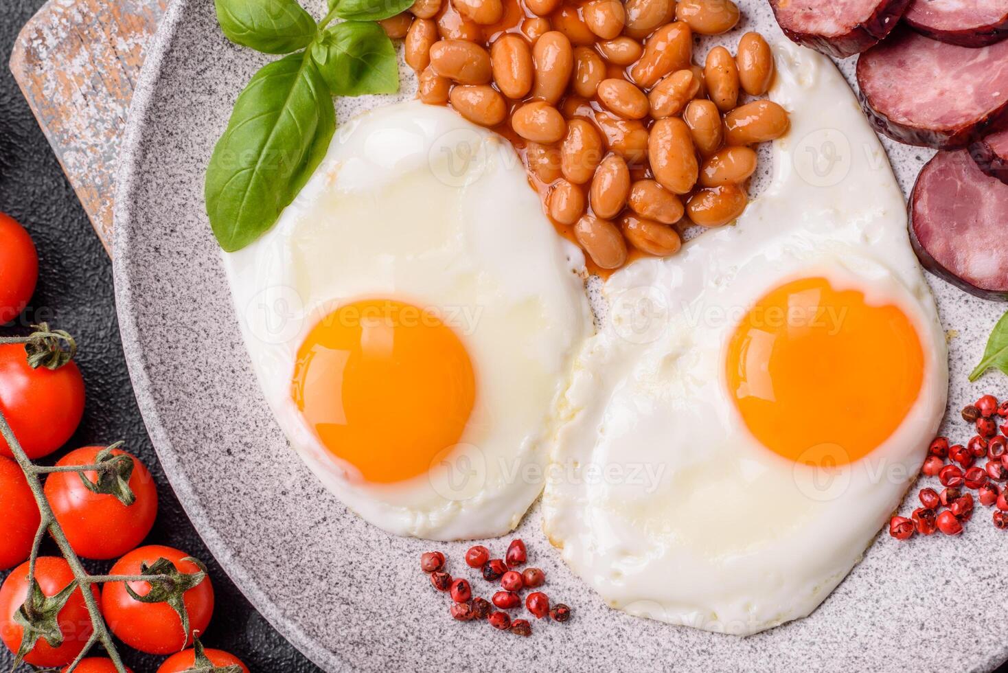 English breakfast with fried eggs, bacon, beans, tomatoes, spices and herbs photo