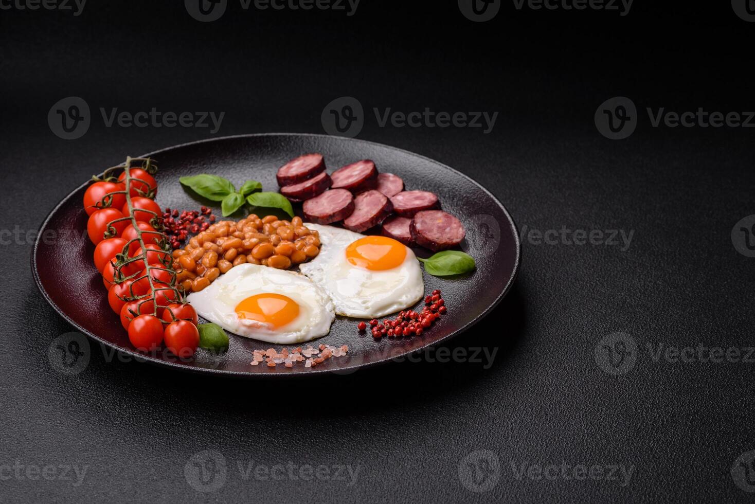 English breakfast with fried eggs, bacon, beans, tomatoes, spices and herbs photo