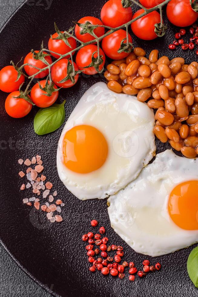 English breakfast with fried eggs, bacon, beans, tomatoes, spices and herbs photo