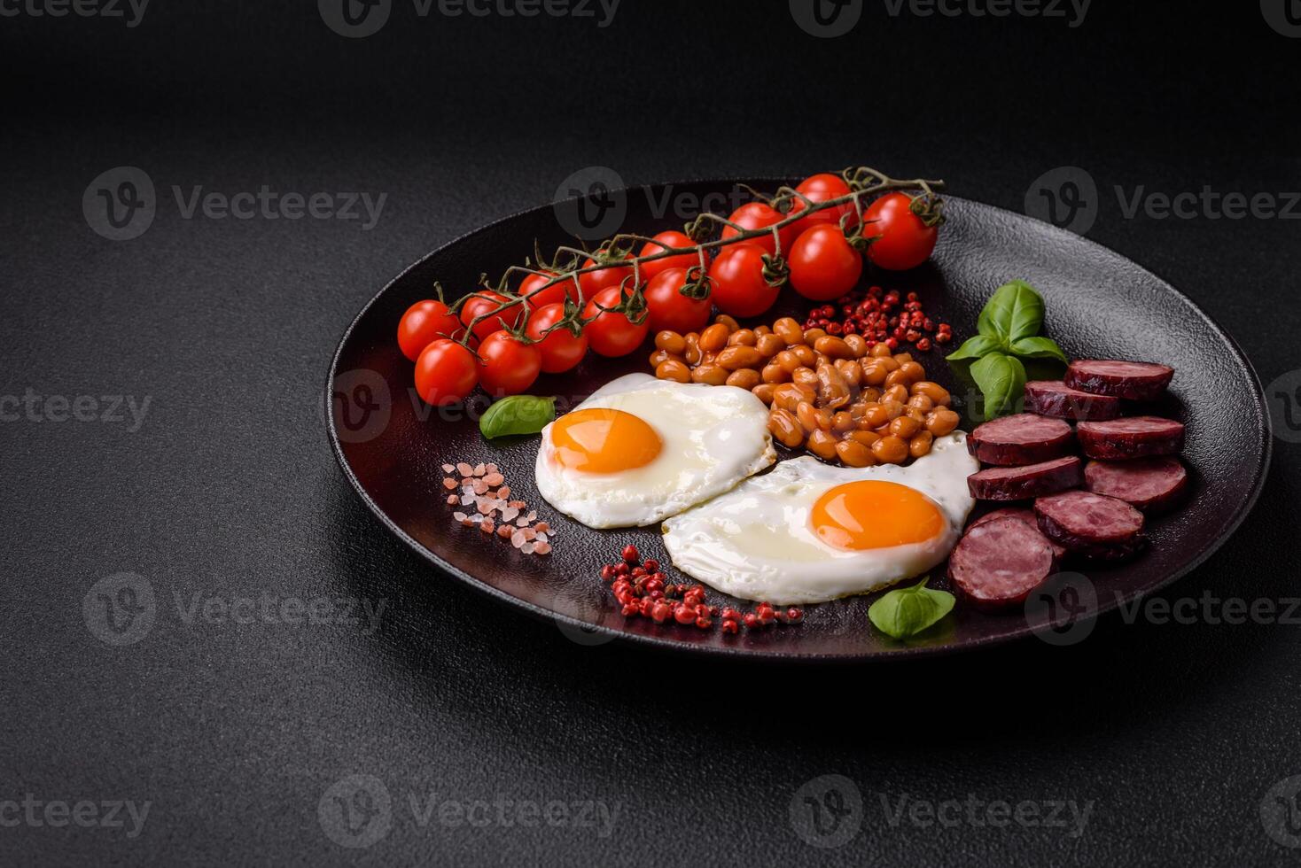 English breakfast with fried eggs, bacon, beans, tomatoes, spices and herbs photo