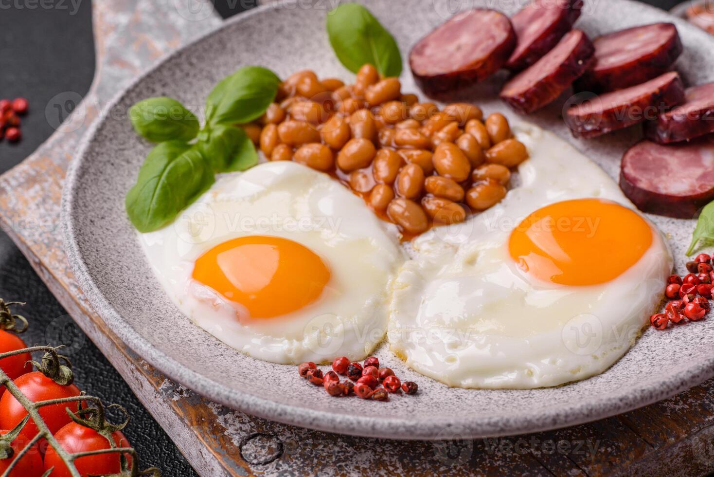 English breakfast with fried eggs, bacon, beans, tomatoes, spices and herbs photo