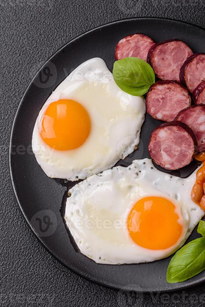 English breakfast with fried eggs, bacon, beans, tomatoes, spices and herbs photo