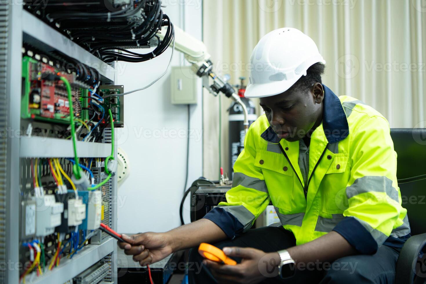 Portrait of a technician working with a digital multimeter to test the electrical system of a huge circuit board at an industrial plant using an automated hand robot. photo