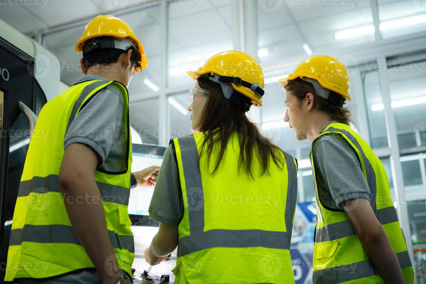 Back view of group young factory worker wearing a hard hat looking at a computer screen used to control production. photo