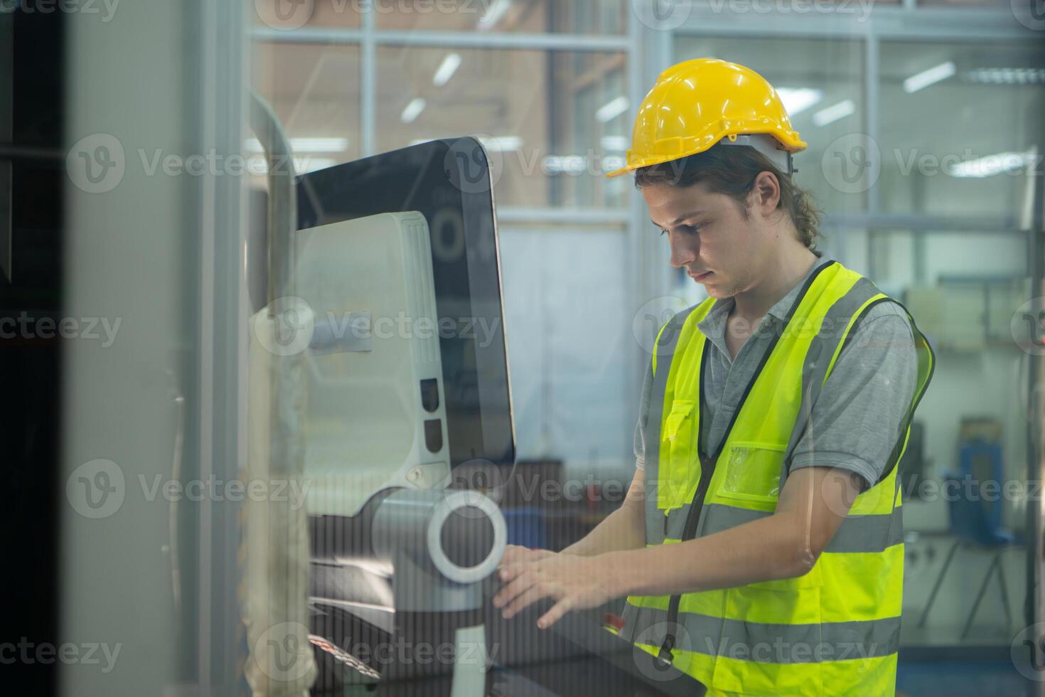 Young man factory worker wearing a hard hat looking at a computer screen used to control production. photo