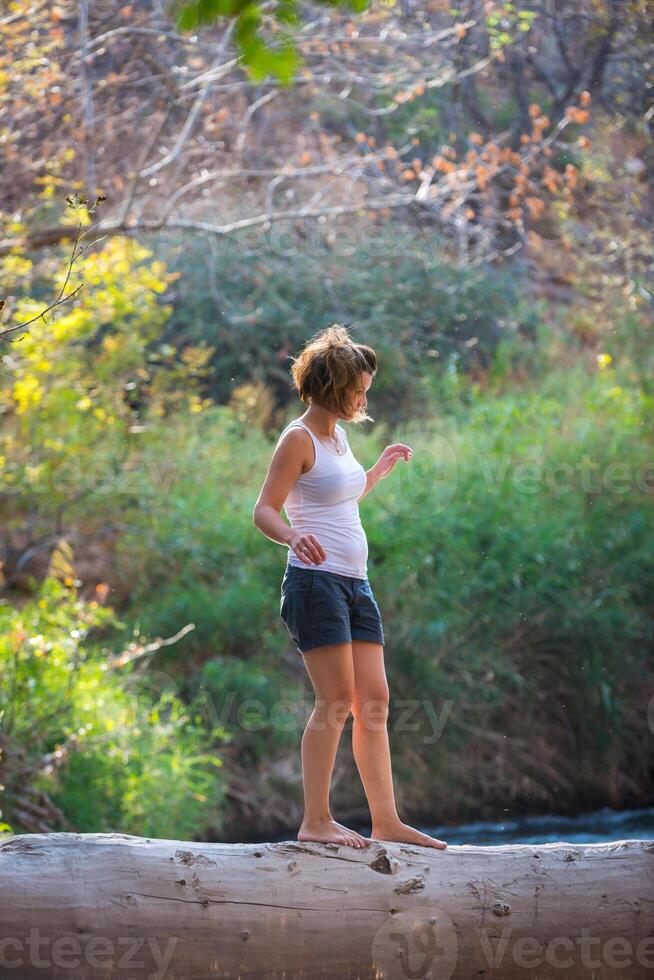 Happy young woman posing on a log over a river photo