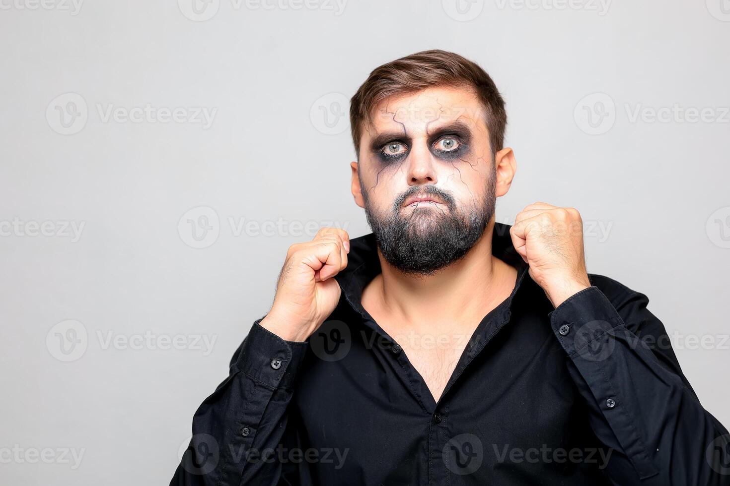a man in a black shirt stands on a white background who has undead-style makeup for Halloween photo