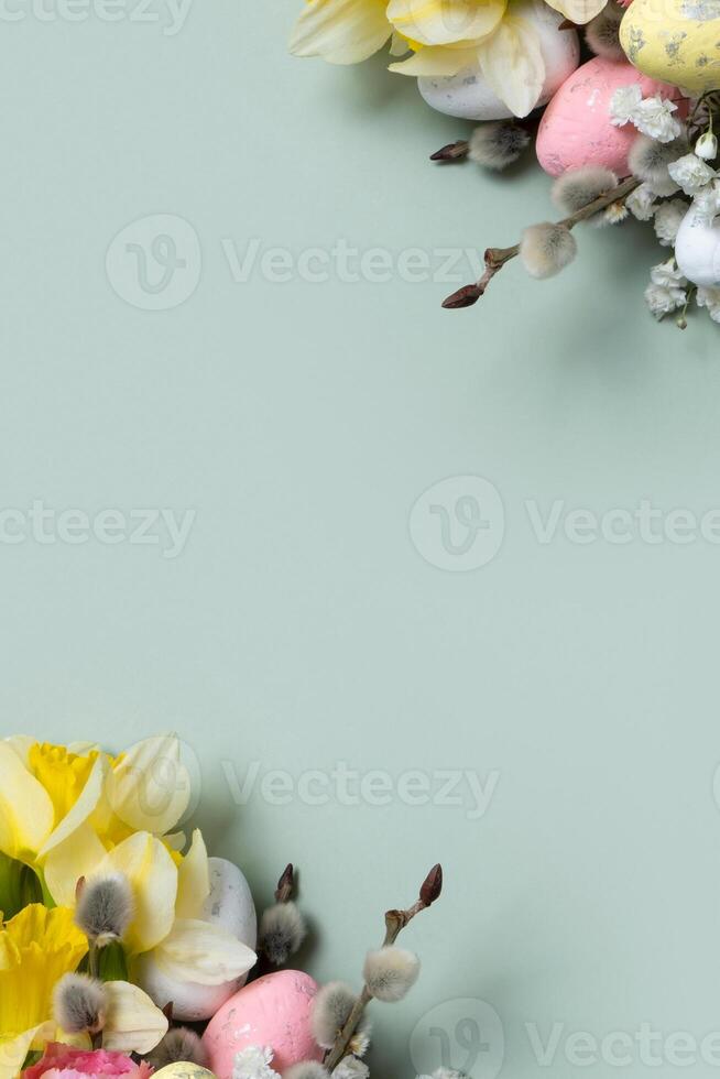Daffodils, easter eggs and willow on green background with copy space. Easter greeting card template vertical format photo