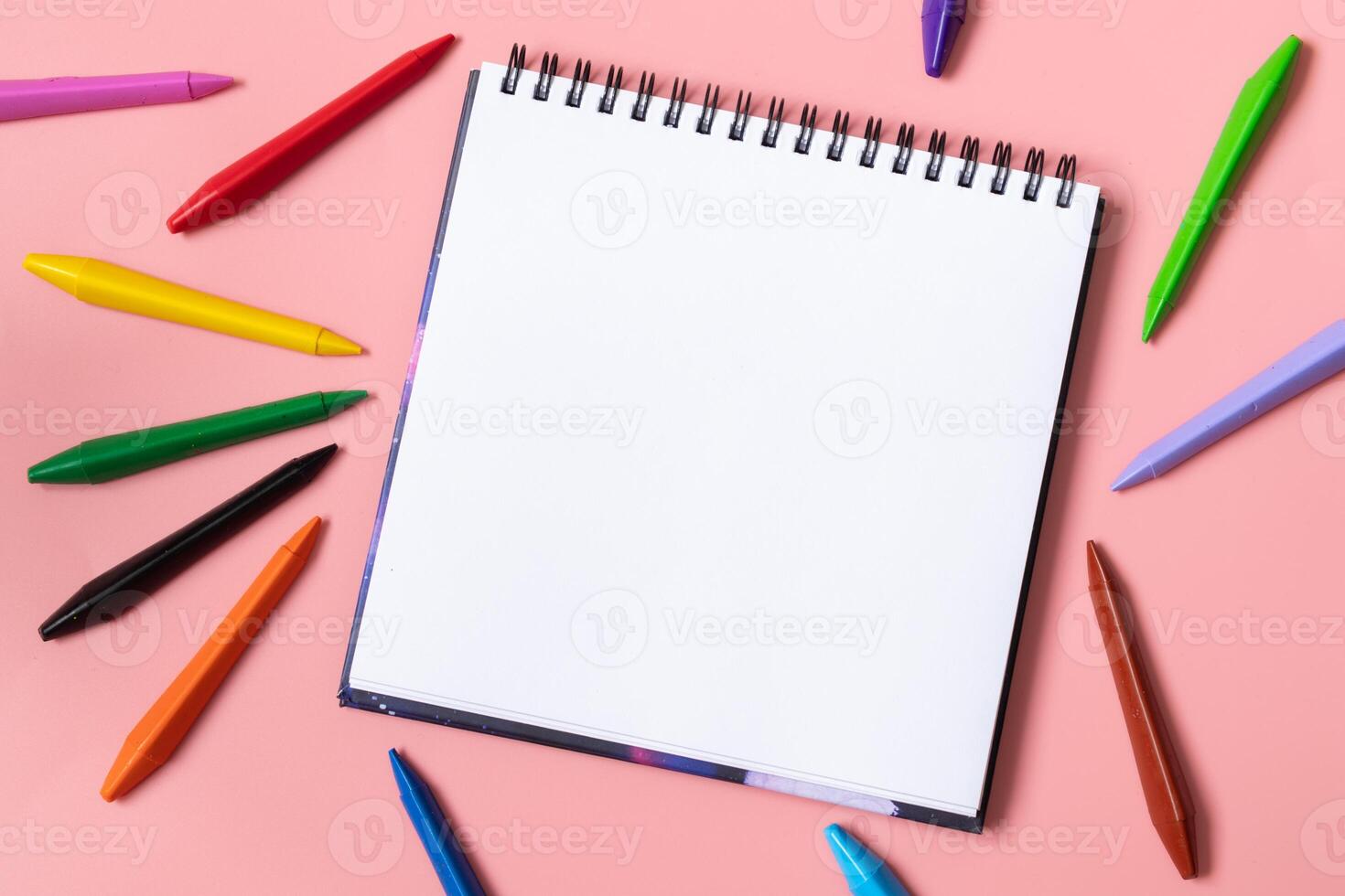 Open sketchbook with white empty blank. Colorful wax crayons on the pastel pink background. Flat lay composition. photo