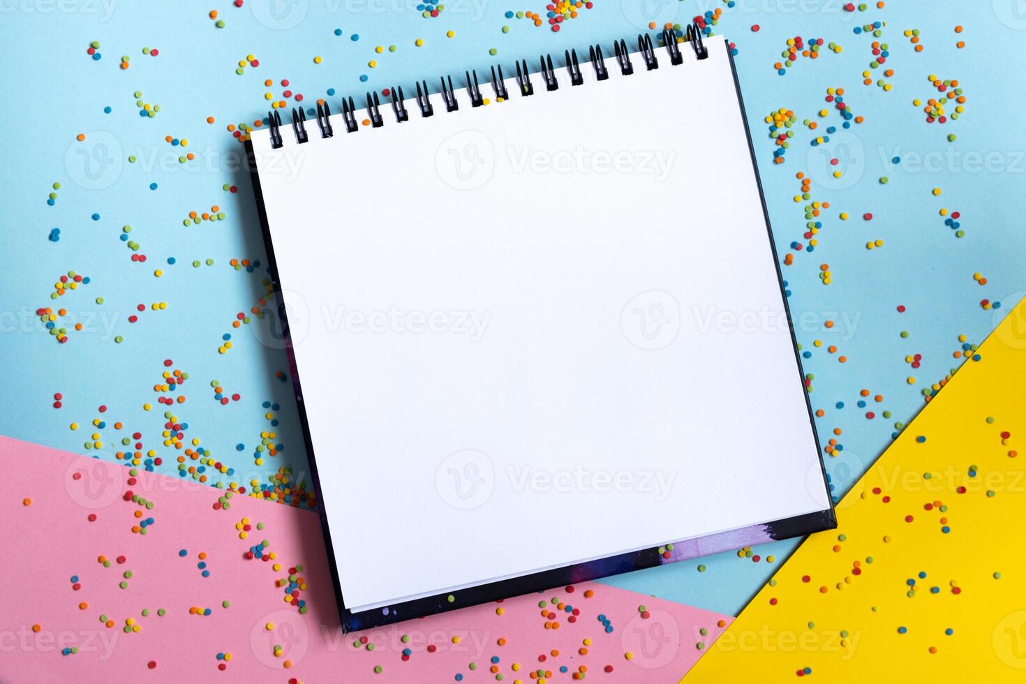 Mock up of empty spiral scketchbook with white paper on bright vibrant background with colorful confetti . Copy space. photo
