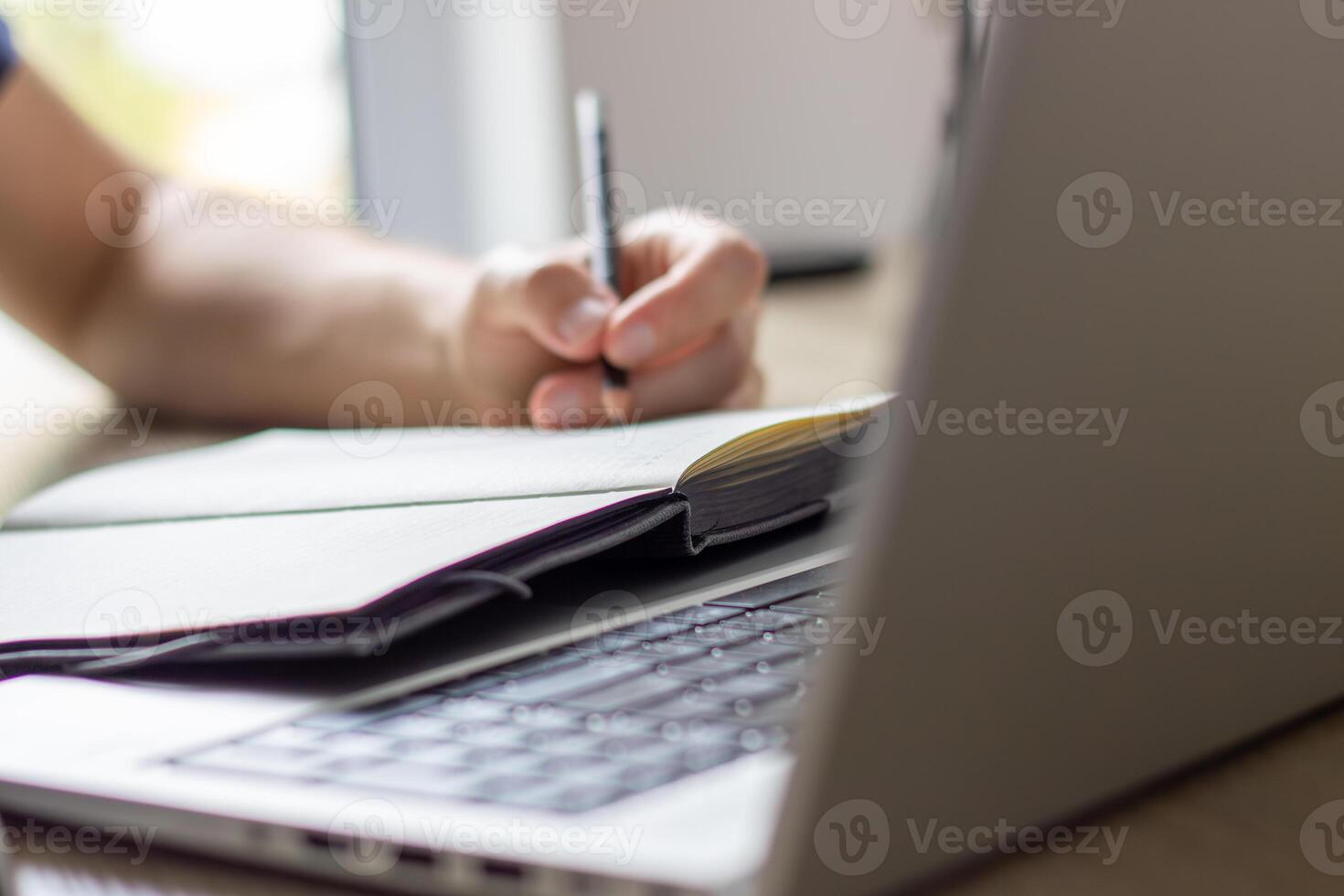 man makes notes in a notebook ,typing in laptop ,at a table, photo