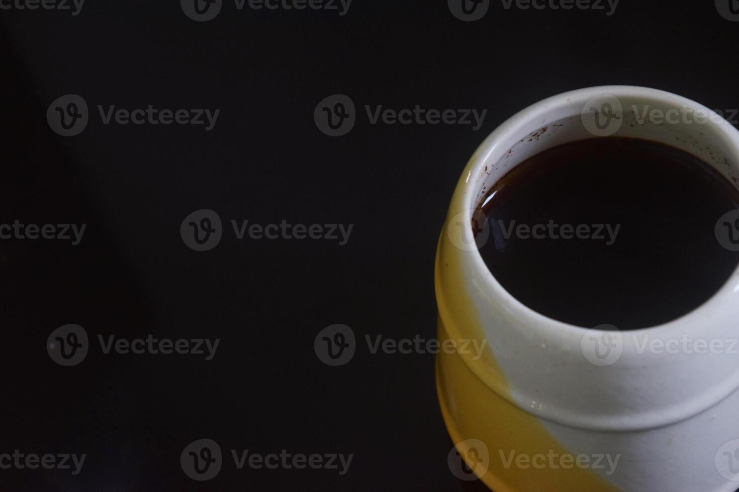 Side view photo of Black coffee in a white and yellow cup on a black ceramic table