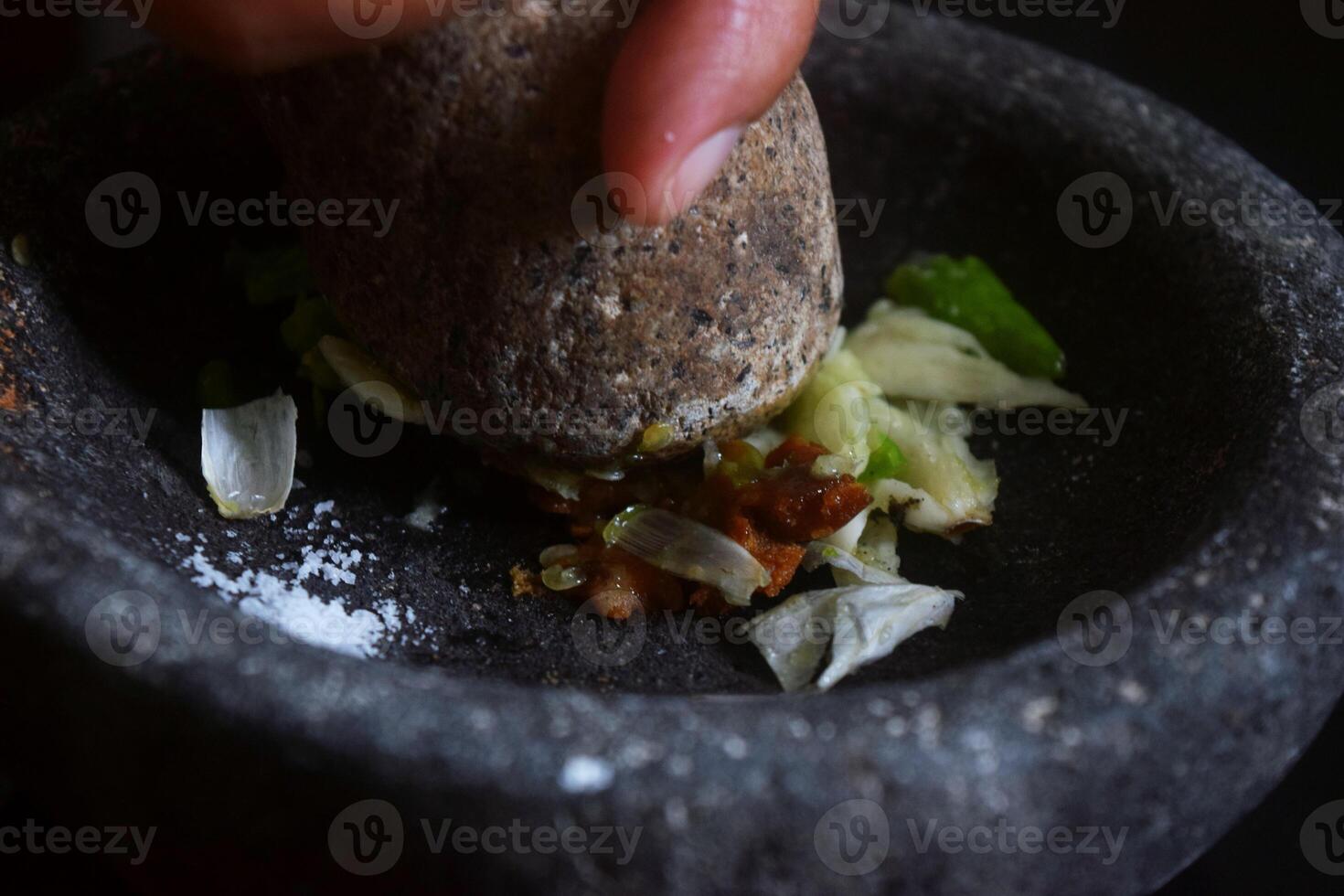Someone is making chili sauce using a stone blender called Cobek photo