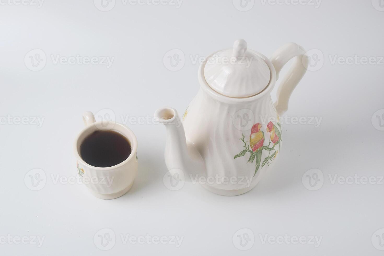 A cup of sweet tea with a ceramic teapot with a bird on a white background photo