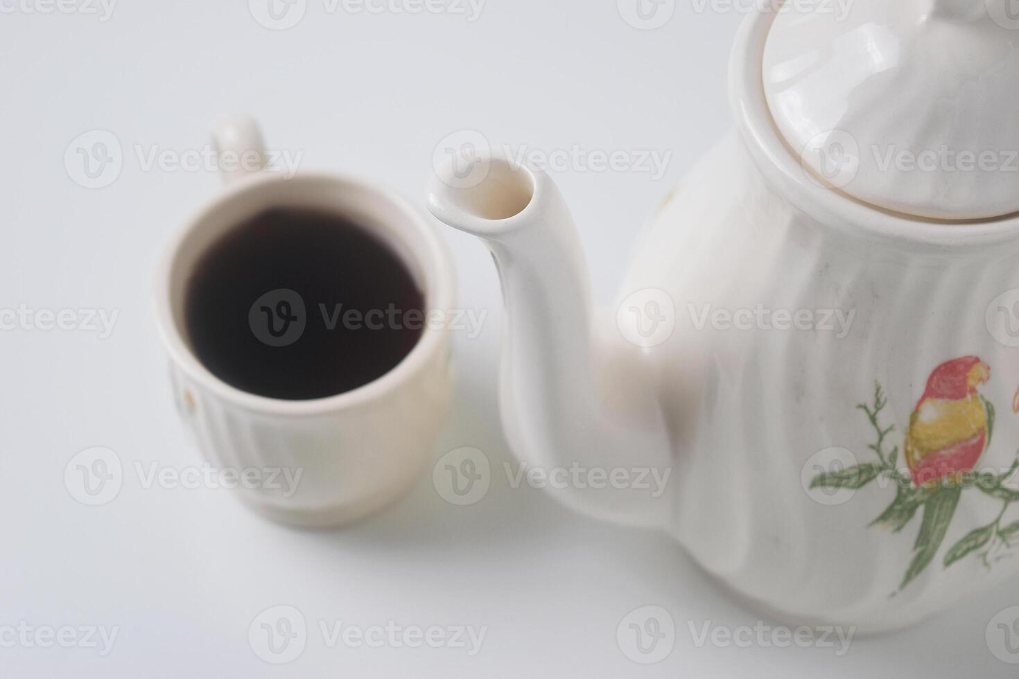 Close up photo of a cup of sweet tea and a white teapot with ceramic material
