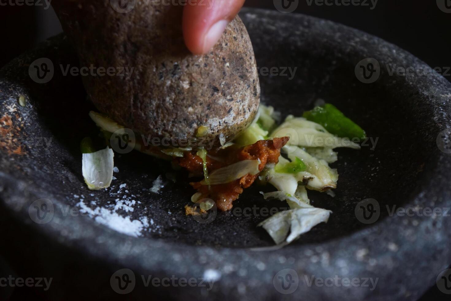 Someone is making chili sauce using a stone blender called Cobek photo