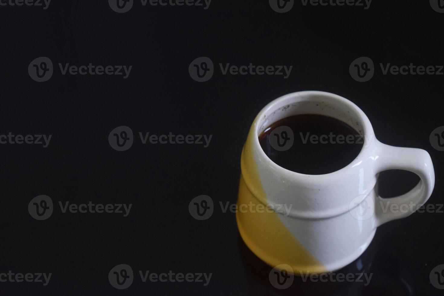 Side view photo of Black coffee in a white and yellow cup on a black ceramic table