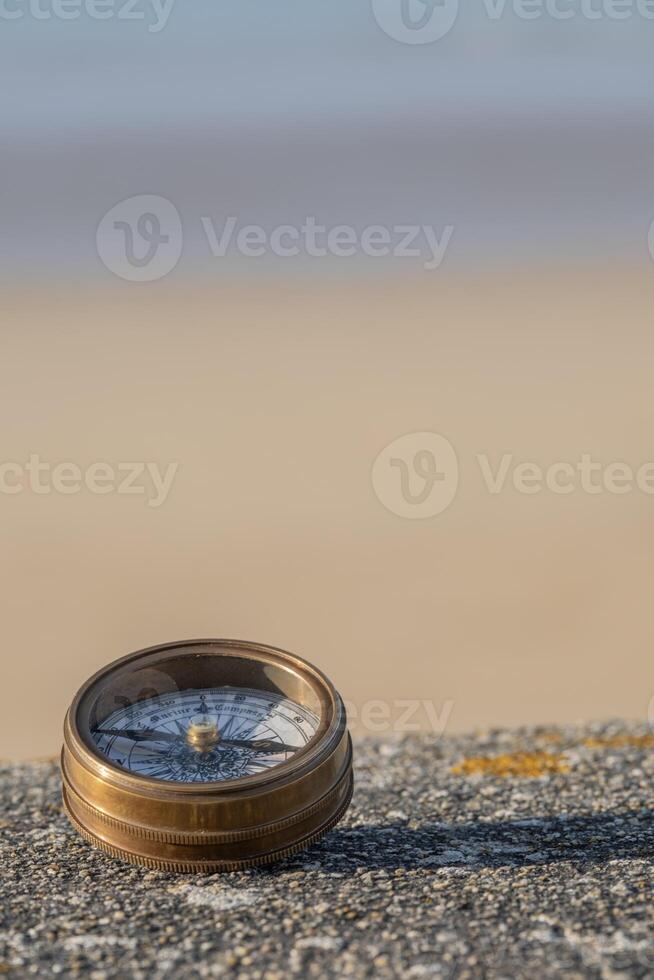 Compass on stone ledge overlooking ocean sand and sky in bakground. Background image photo
