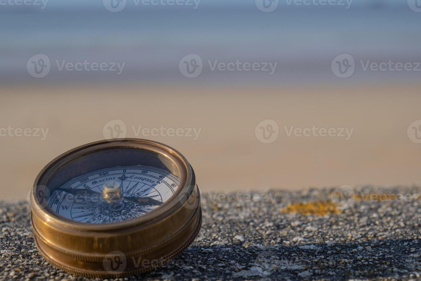 Compass on stone ledge overlooking ocean sand and sky in bakground. Background image photo