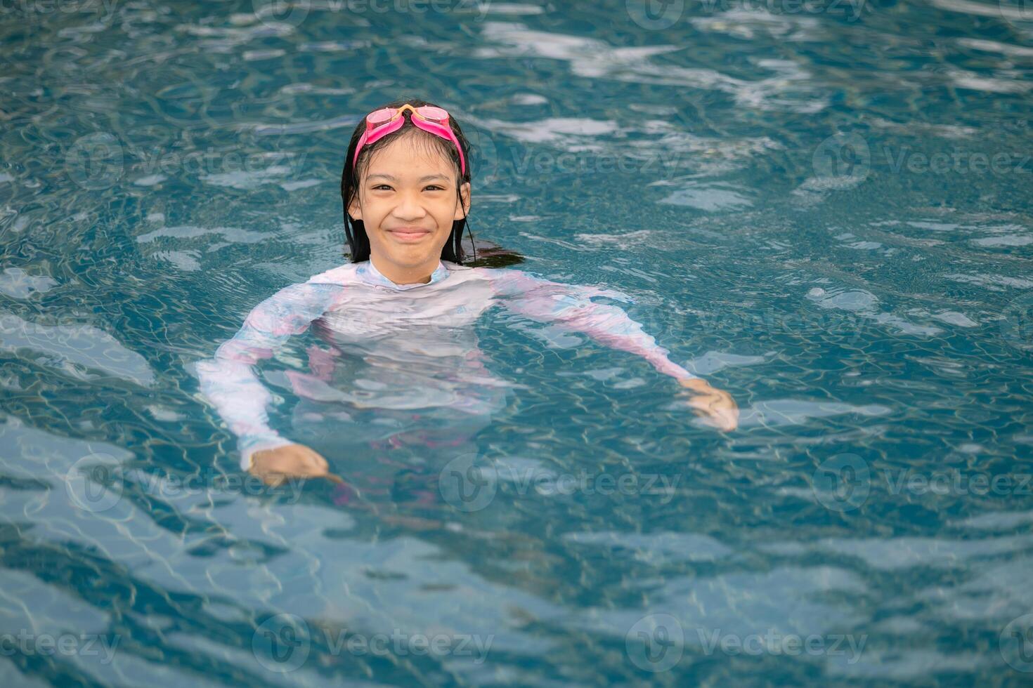 A young girl is in the water wearing a white shirt and pink goggles photo