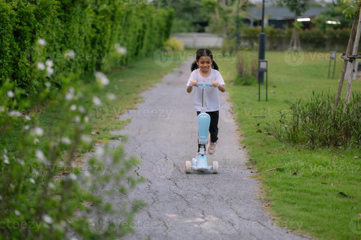 A young girl riding a blue scooter down a path photo