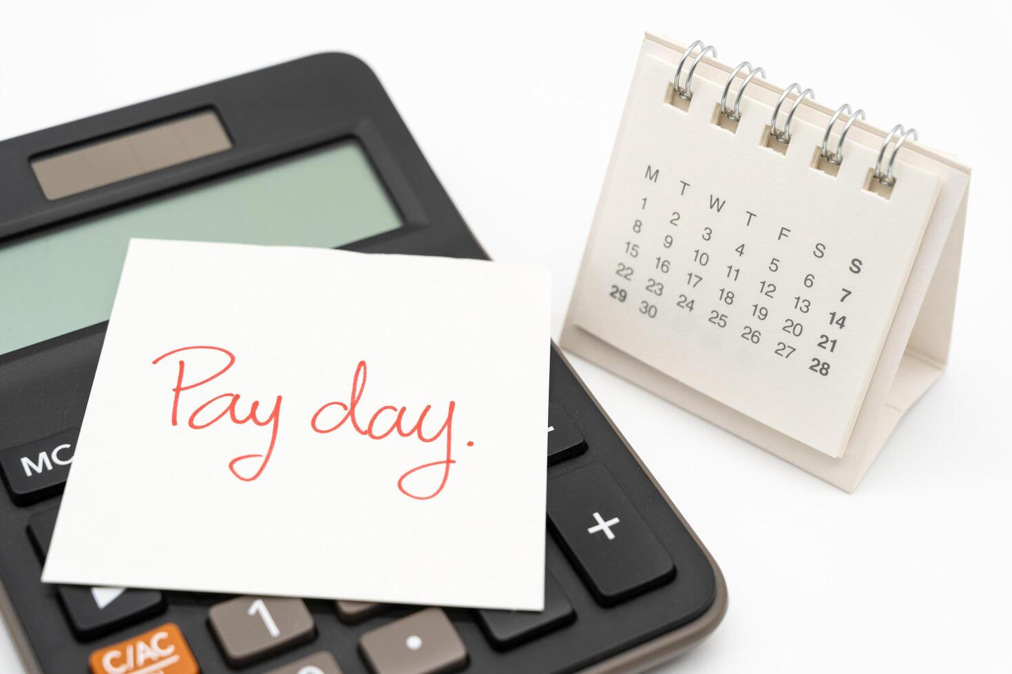 For payday concept. Desk calendar, calculator and paper note in isolated background. Business, finance, savings money, wages, payroll or accounting concept. photo