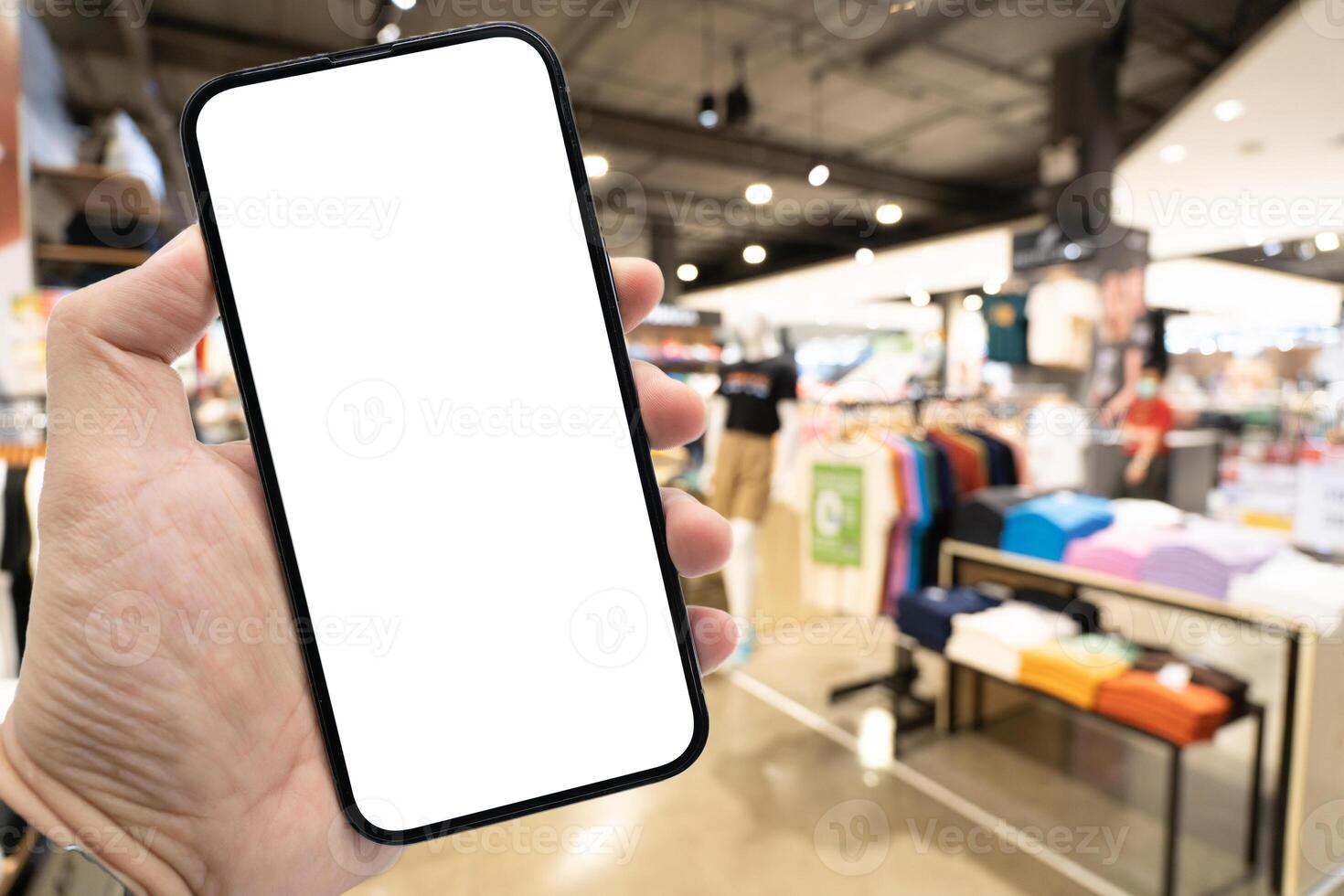 Hand holding blank screen smartphone for copy space on blurred clothing store. e-commerce app shopping mockup. social media, payment and shopping online concept. fashion and technology. photo