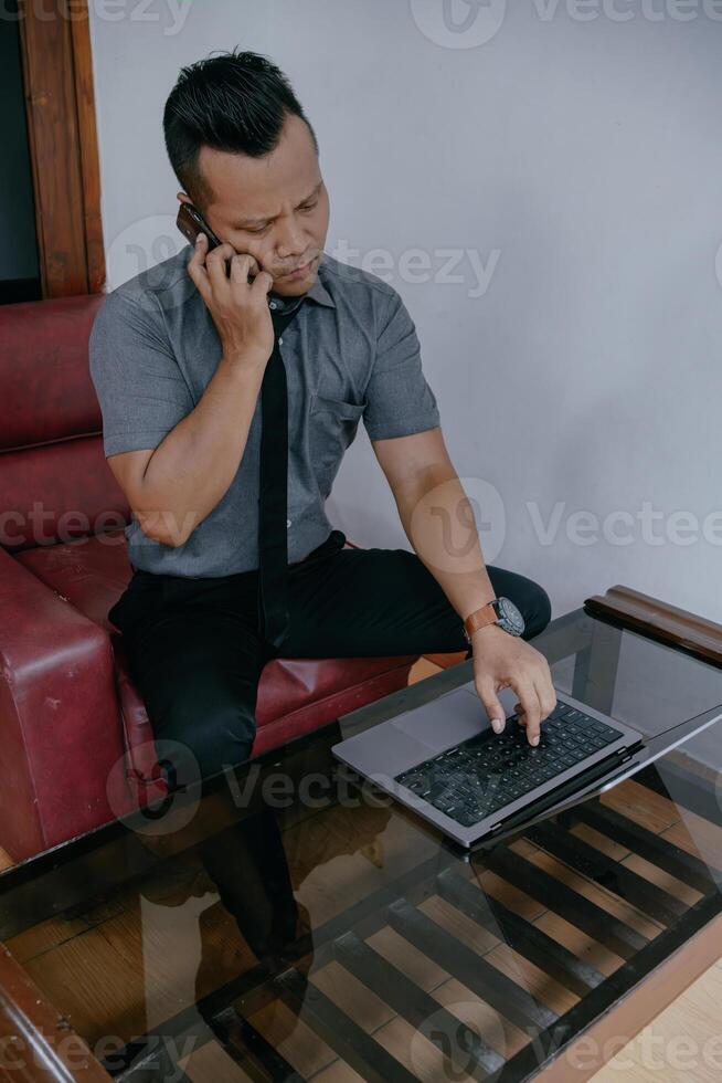 Young Indonesian man talking on mobile phone sitting on sofa at home. photo