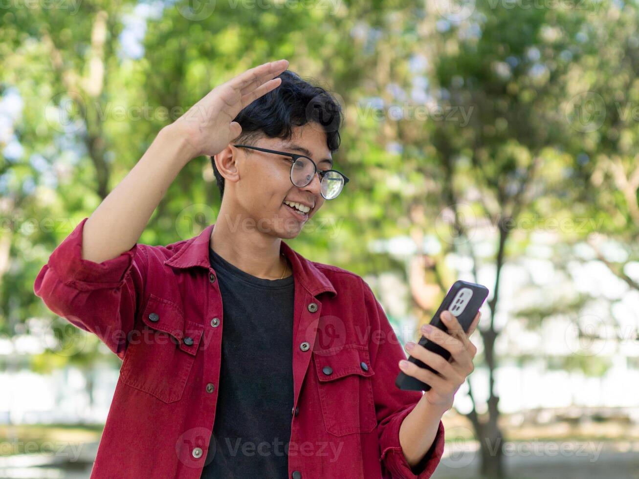 Asian man holding handphone and calling with friends waving hand making hello gesture. Man using smartphone for online conference call photo