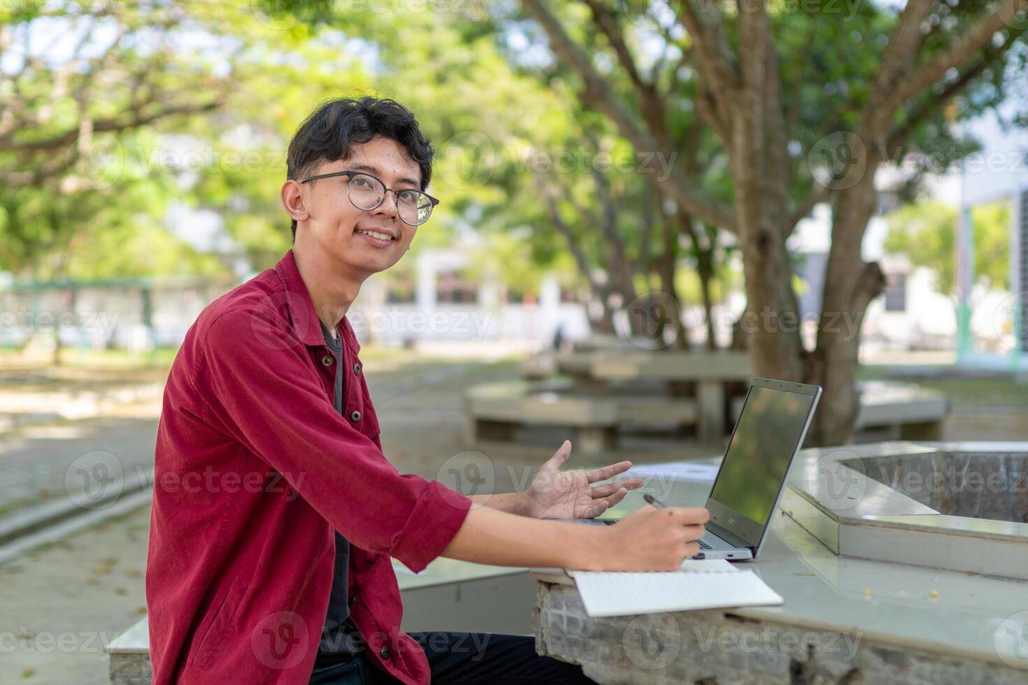 Portrait of Asian college student using laptop looking to camera. A man working with a laptop computer at campus photo