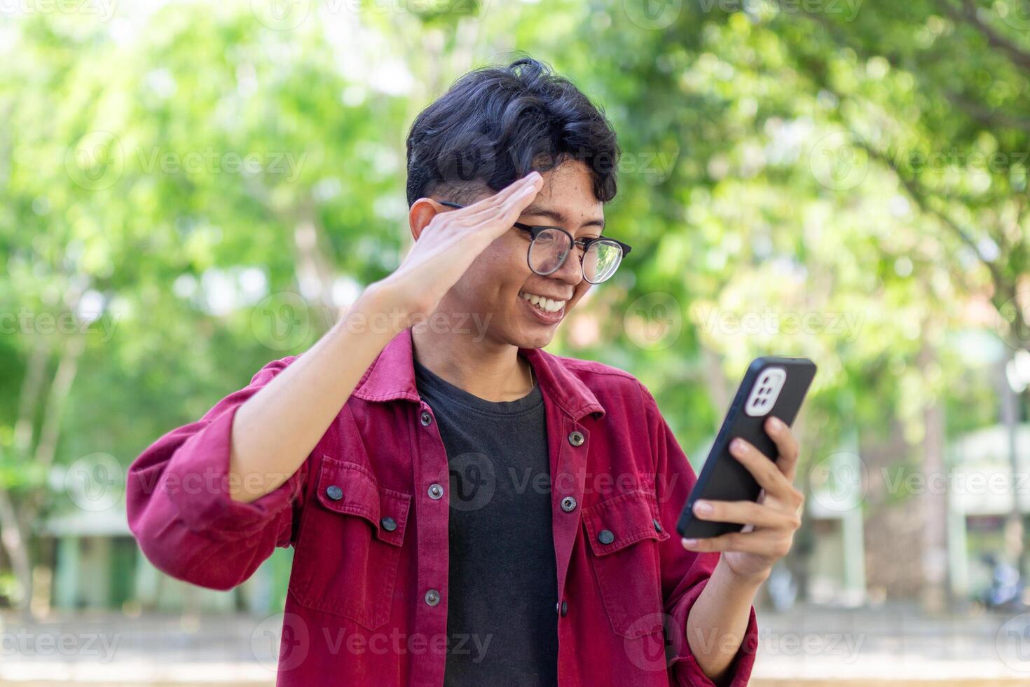 Asian man holding handphone and calling with friends waving hand making hello gesture. Man using smartphone for online conference call photo