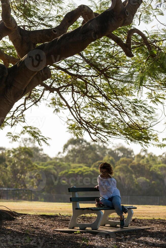Girl sitting on a bench under a big tree photo