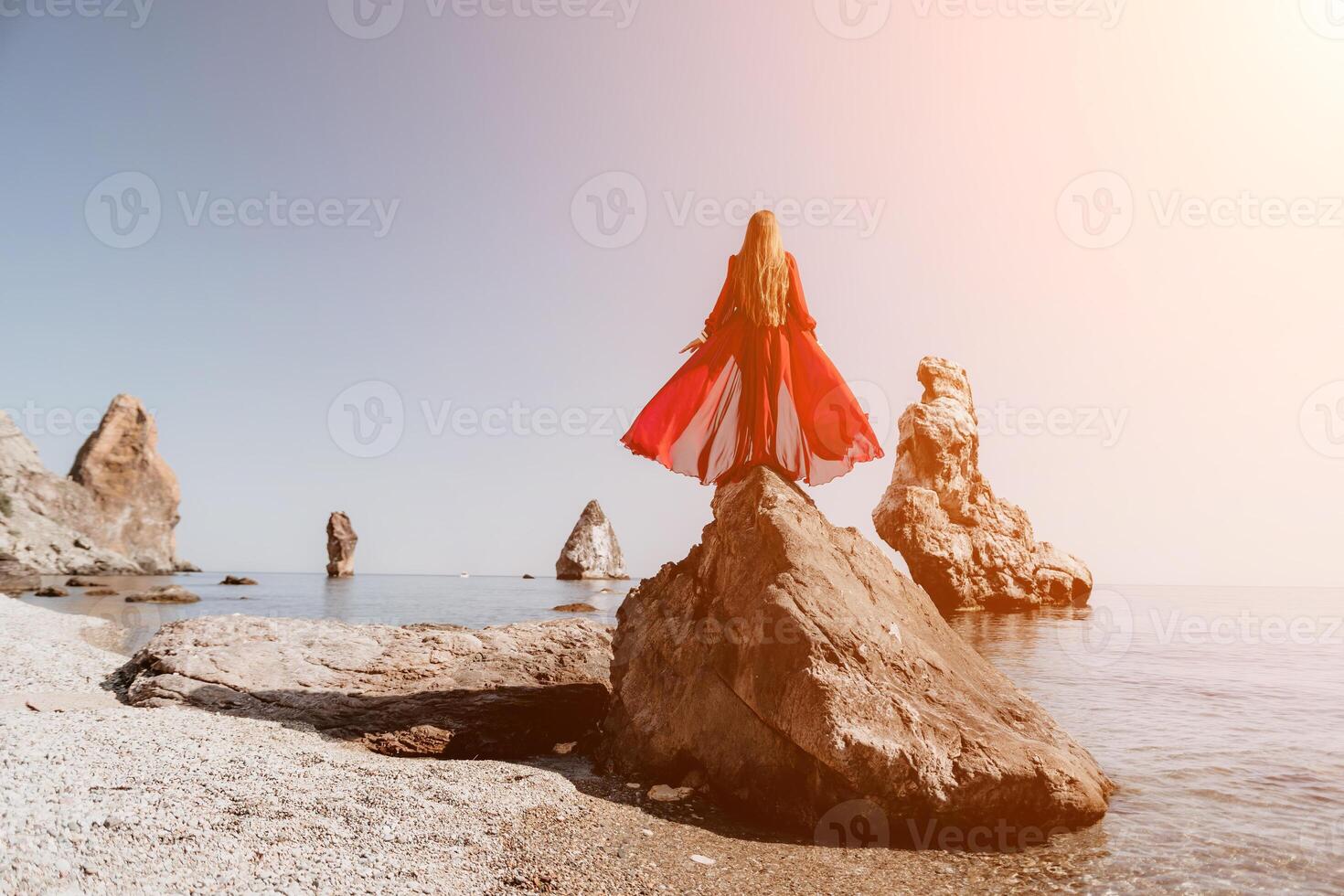 Woman travel sea. Young Happy woman in a long red dress posing on a beach near the sea on background of volcanic rocks, like in Iceland, sharing travel adventure journey photo