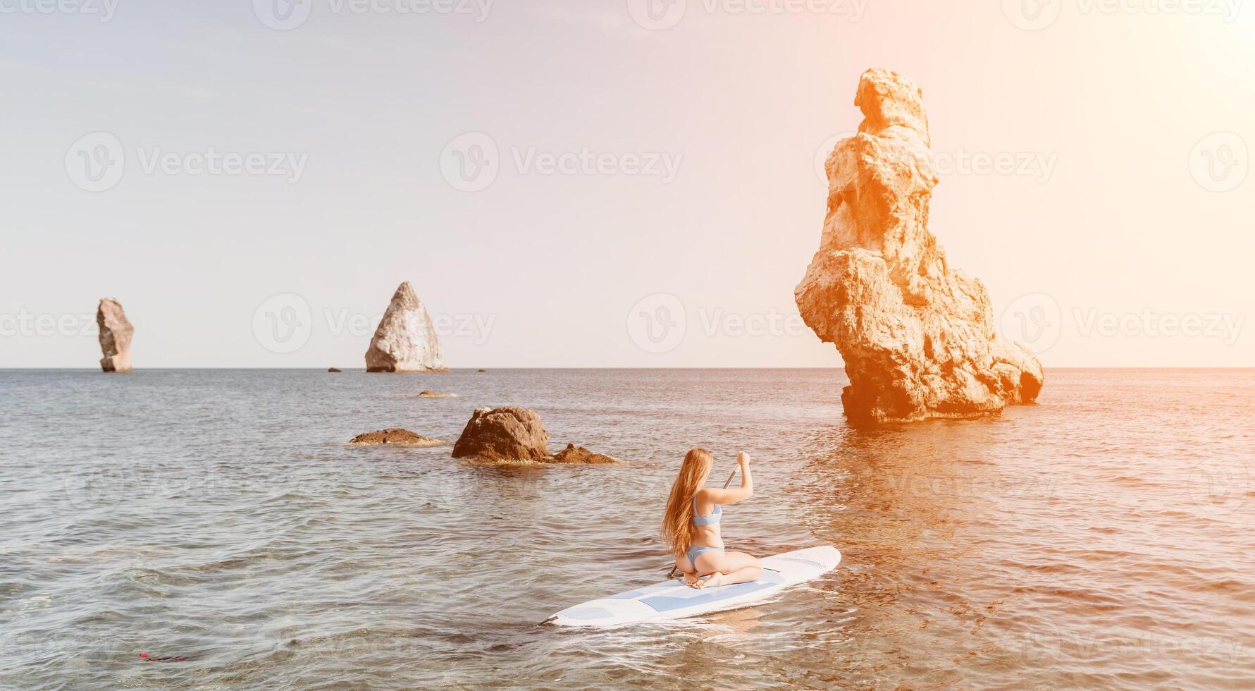 Woman sea sup. Close up portrait of happy young caucasian woman with long hair looking at camera and smiling. Cute woman portrait in a blue bikini posing on sup board in the sea photo