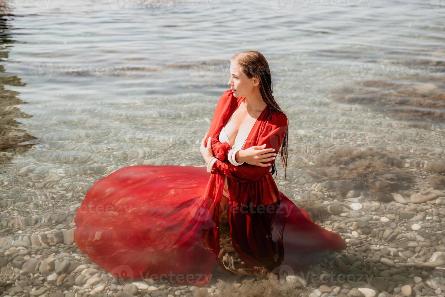 Woman travel sea. Happy tourist in red dress enjoy taking picture outdoors for memories. Woman traveler posing in sea beach, surrounded by volcanic mountains, sharing travel adventure journey photo