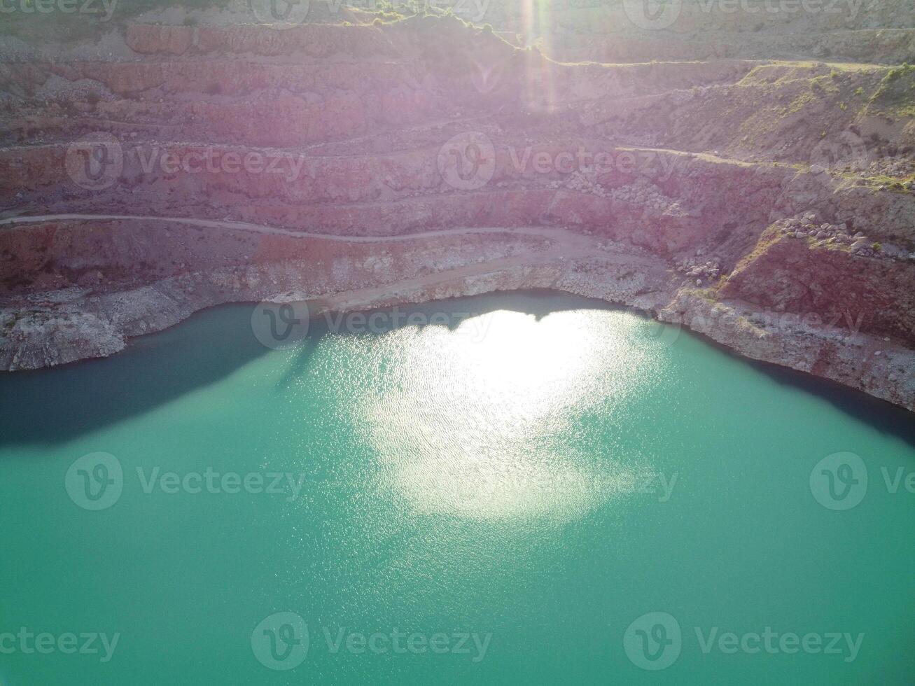 Aerial top view on opencast mining quarry with flooded bottom, turquoise surface of the lake. Quarry pond overgrown with green plants and clear turquoise water photo