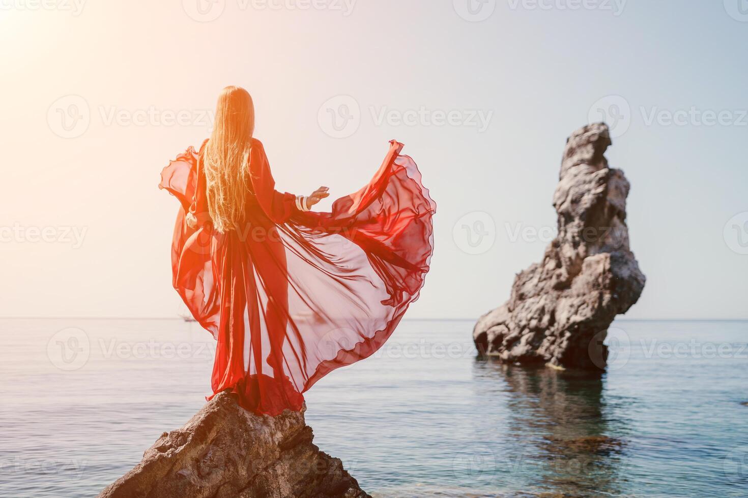 Woman travel sea. Young Happy woman in a long red dress posing on a beach near the sea on background of volcanic rocks, like in Iceland, sharing travel adventure journey photo