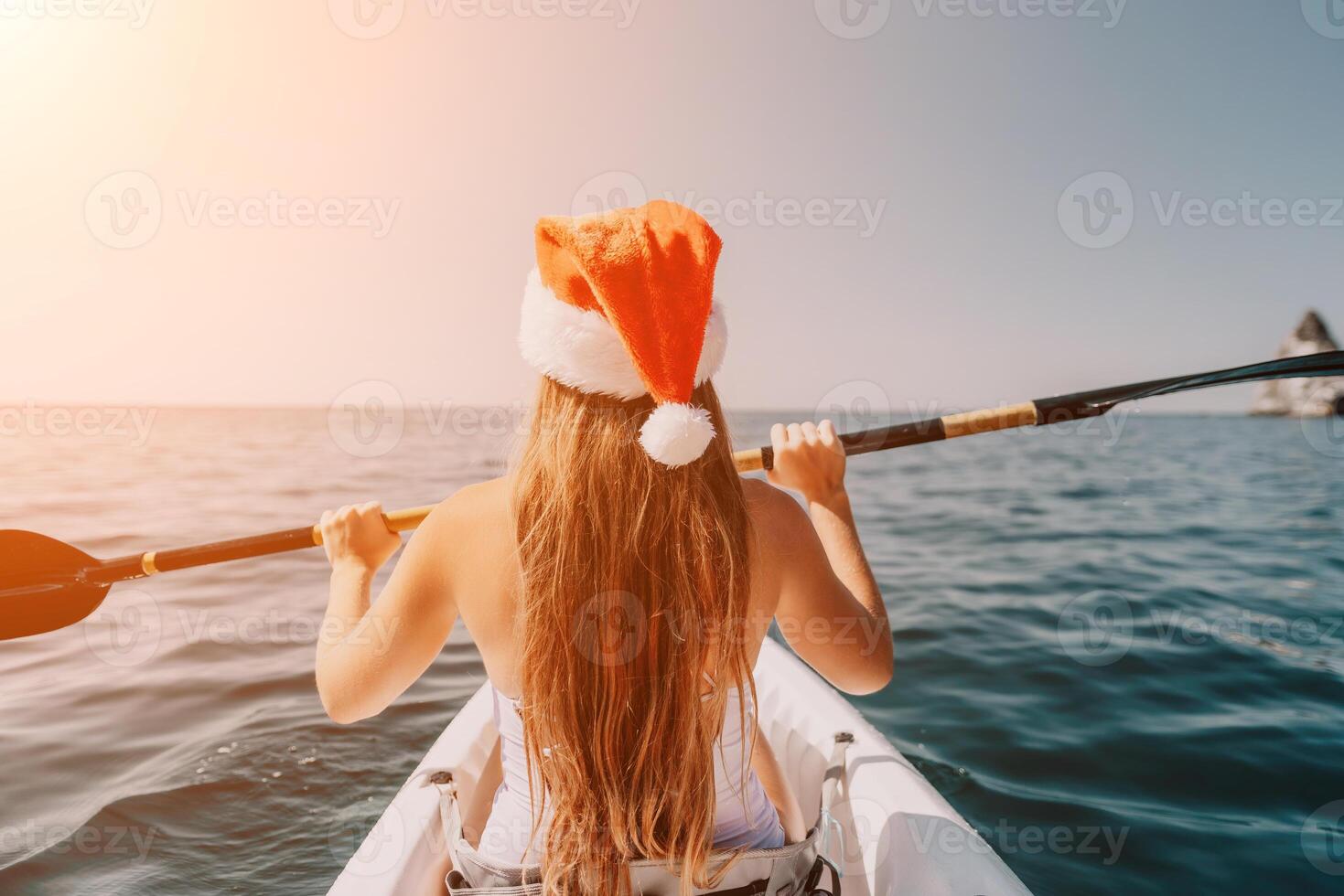 Woman in kayak back view. Happy young woman in Santa hat floating in kayak on calm sea. Summer holiday vacation and cheerful female people relaxing having fun on the boat. photo